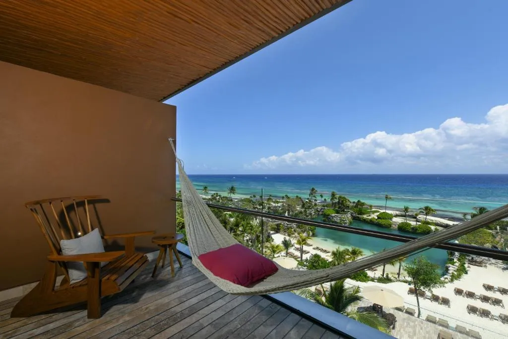 Balcón del Hotel Xcaret México con hamaca, sillón de madera y vista panorámica al mar Caribe y playas privadas.