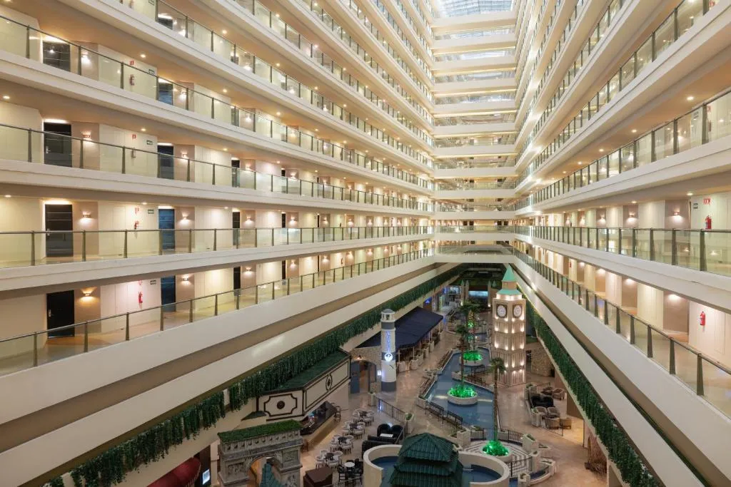 Interior del Seadust Cancún Family Resort con múltiples pisos, pasillos iluminados y área central con fuentes decorativas.